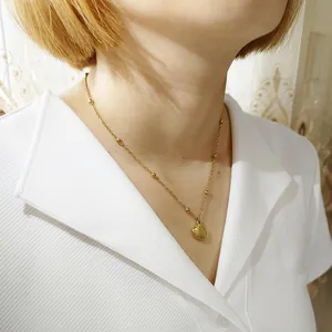 Detalle de un collar con colgante de concha dorada sobre una camisa blanca con cuello.