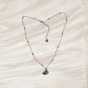 Vista detallada de un collar con colgante de concha de acero sobre seda plisada elegante