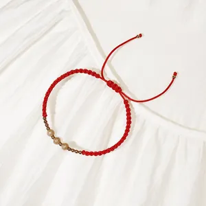 Dettaglio di un bracciale in corda rossa intrecciata con perle dorate in acciaio sabbiato