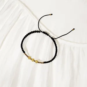 Dettaglio di un bracciale intrecciato nero con perline in acciaio inossidabile oro opaco.