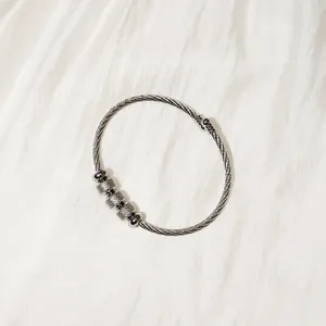 Detail view of a silver stainless steel twisted wire bangle with textured metal beads.