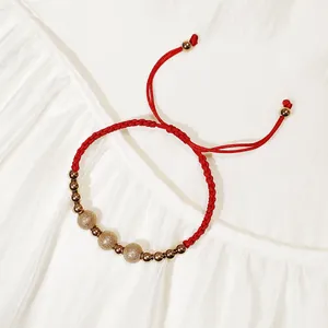 Vista dettagliata del bracciale intrecciato rosso con perle dorate sabbiate e lisce