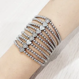 Close-up of heart-shaped letter charms on silver stainless steel beaded elastic bracelets