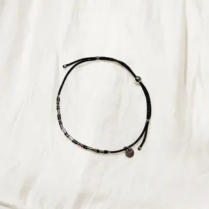 Détail d'un bracelet en cordon noir avec des perles en acier inoxydable et breloque.
