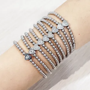 Close-up view of silver stainless steel beaded bracelets with engraved heart charms on wrist