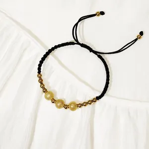 Dettaglio di bracciale in cordino nero intrecciato con perle dorate sabbiate e lucide.