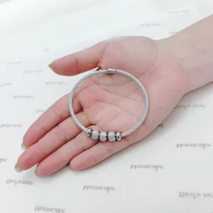 Macro view of a silver stainless steel cable wire bracelet with beads on a human palm.