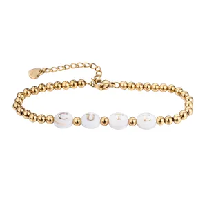 Makroaufnahme eines vergoldeten Perlenarmbandes aus Edelstahl mit weißen CUTE-Muschelbuchstaben