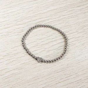 Detail view of a silver stainless steel beaded bracelet with a heart initial 'E' charm.