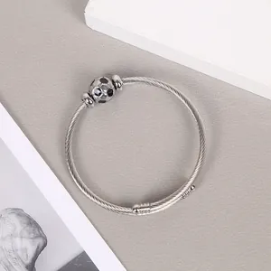 Detail view of a silver stainless steel cable bangle with a metallic soccer ball charm.
