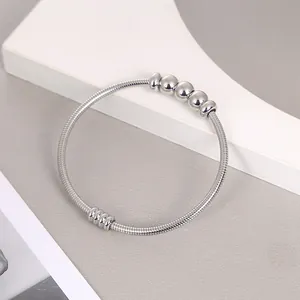 Detalle de un brazalete de resorte de acero inoxidable plateado con cuentas móviles.
