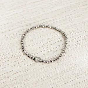 Detailed macro view of the heart charm engraved with letter W on a silver beaded bracelet