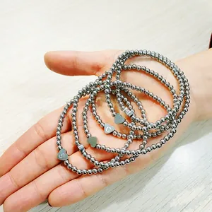 Close-up of silver stainless steel beaded bracelets with engraved heart charms on a hand.