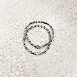 Macro detail of stainless steel beaded bracelets featuring engraved heart charms