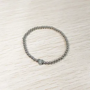 Detail view of a silver heart-shaped initial S stainless steel beaded elastic bracelet