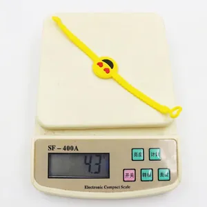Close-up detail of a yellow PVC cartoon emoji bracelet being weighed on a scale