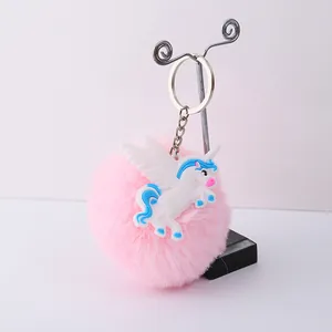 Détail d'un porte-clés à pompon rose avec une jolie breloque licorne en PVC blanc.
