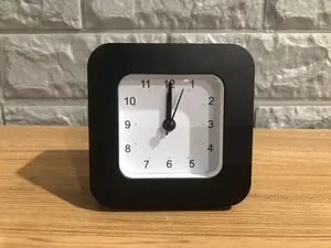 Detailed close-up view of a minimalist square black analog alarm clock on a wooden desk