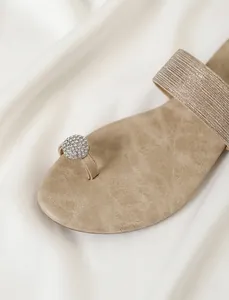 Détail de sandale plate avec décor de strass et texture en cuir beige doux.