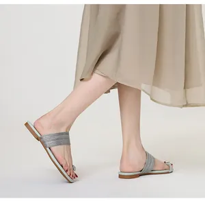 Détail de marche en sandales plates à strass avec une jupe plissée beige.