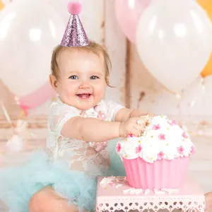 Pink glitter pet birthday hat shown on a baby model with party decorations and cake