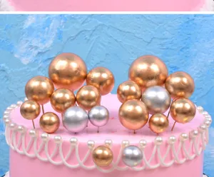 Close-up detail of gold and silver metallic ball cake toppers on a pink festive cake