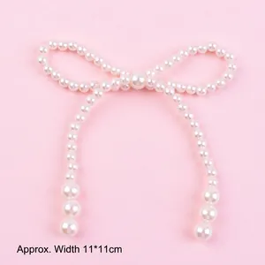 Detailed close-up of a decorative white pearl bow cake topper on a soft pink surface