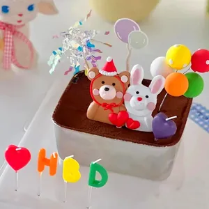 Candele di compleanno colorate a forma di lettere HBD e cuore su una torta decorata.