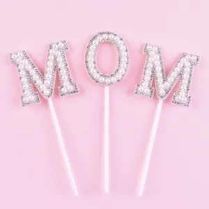 Détail de la décoration de gâteau MOM en perles et strass sur un joli fond rose