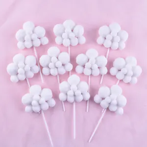 Detailed view of ten white fluffy pom-pom cloud cake toppers on a pink backdrop.