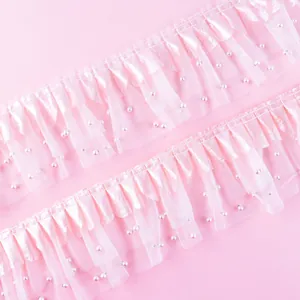 Macro detail of pink ruffled lace ribbon with small pearls for elegant cake decoration.