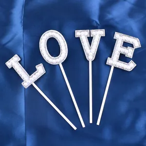 Close-up detail of elegant pearl-studded LOVE letter cake toppers on blue silk cloth