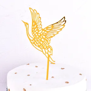 Detailed view of an elegant golden acrylic crane cake topper on a white frosted cake