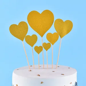 Seven golden glittery heart-shaped cake toppers arranged on a elegant white dessert cake