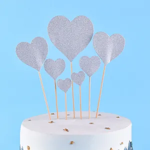Close-up of silver glitter heart cake toppers on a white cake with gold flakes.