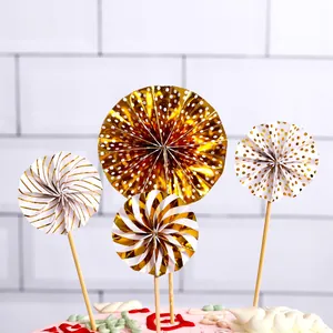Set of 4 gold and white paper fan cake toppers with dots and stripes for party decor.
