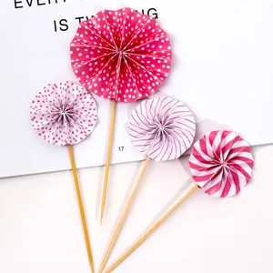 Close-up of four pink and white paper fan cake toppers with polka dots and stripes.