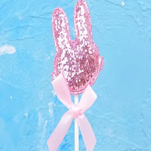 Vista detallada de un topper de conejo rosa brillante para tarta con un lazo de cinta rosa