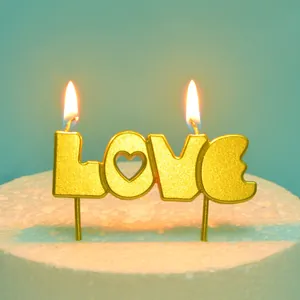 Nahaufnahme einer brennenden goldenen LOVE-Kerze auf einem weißen Kuchenboden vor blau