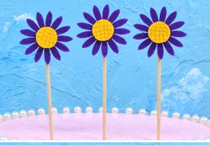 Close-up of three purple felt sunflower cake toppers for birthday party dessert.