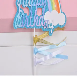 Nahaufnahme eines Regenbogen-Wolken-Kuchenaufsatzes mit Happy Birthday und Bändern.