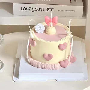 Detailed macro shot of a pink bowknot birthday candle on a cream heart cake decoration