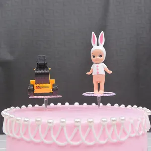 Transparent plastic cake topper bases for doll decorations on a pink cream cake