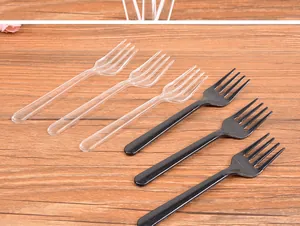 Detail of disposable black and transparent plastic four-tine forks on wooden table