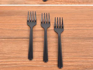 Close-up of three professional disposable black plastic four-tined fruit forks on wooden table