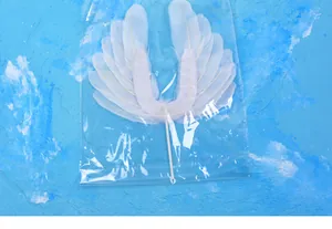 Handcrafted white feather angel wing cake topper decoration shown inside plastic packaging