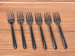 Six black disposable 4-prong plastic dessert forks arranged on a wooden tabletop