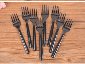 Close-up detail showing multiple disposable black plastic dessert forks on wooden background