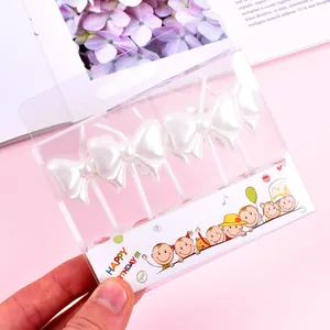 Detailed close-up shot of pearlescent white bow-shaped birthday candles in plastic packaging