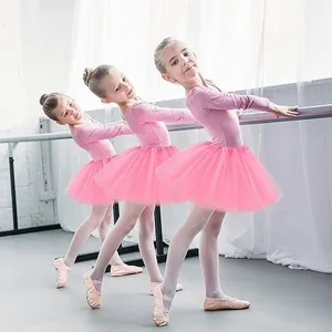 Three young girls in pink ballet tutus practicing at a dance barre in a studio